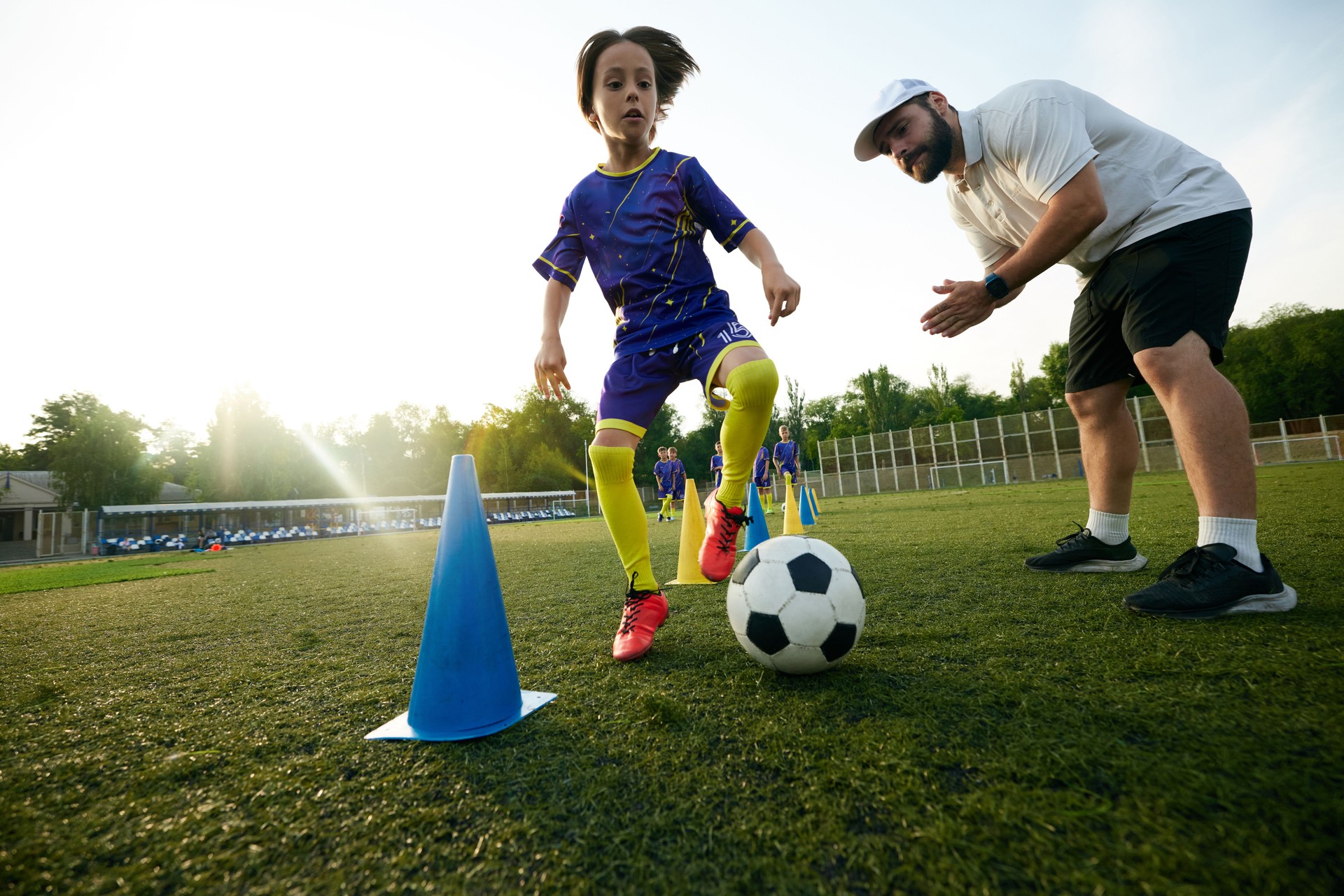 Male sport coach guiding young player through dribbling drill, encouraging and commentating. Focus and concentration